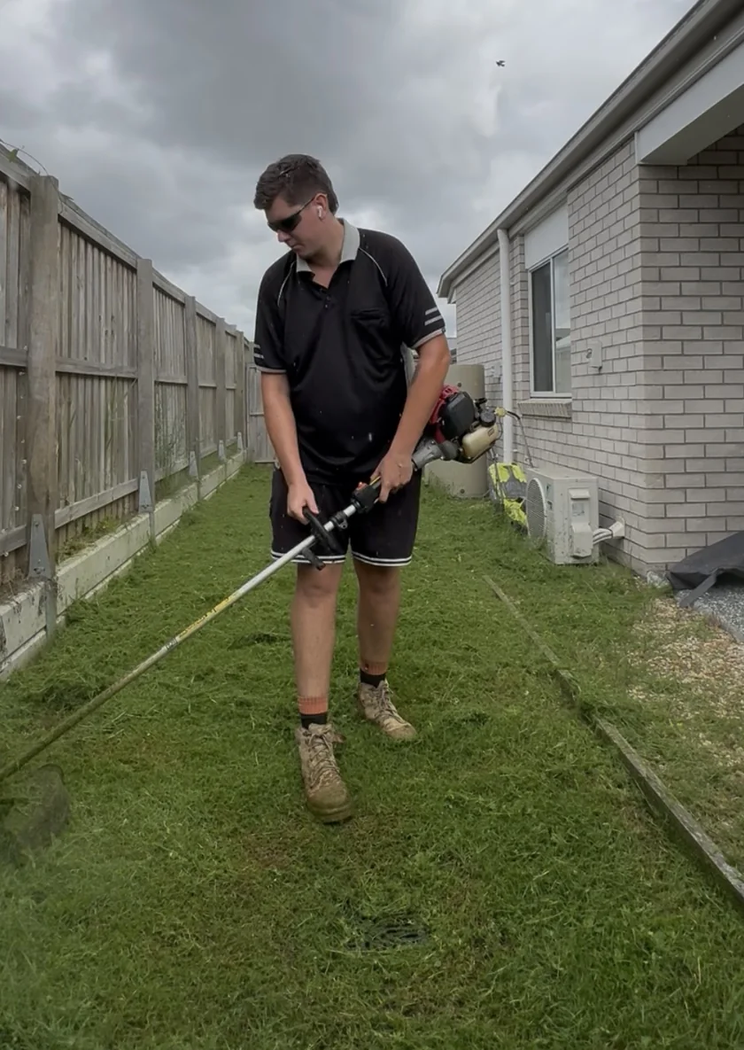 Brandon from Greenstone Outdoor Solutions trimming a residential lawn with a line trimmer